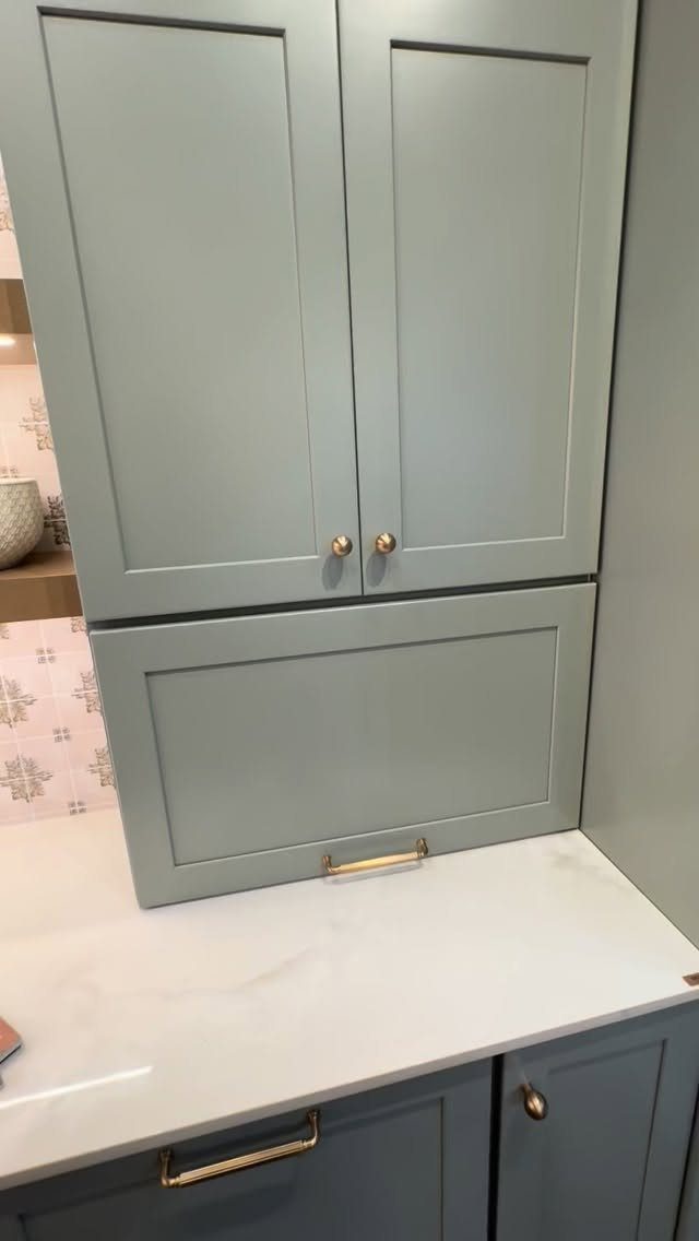 Light blue-grey kitchen cabinets featuring a roll-up appliance garage and white marble countertop.