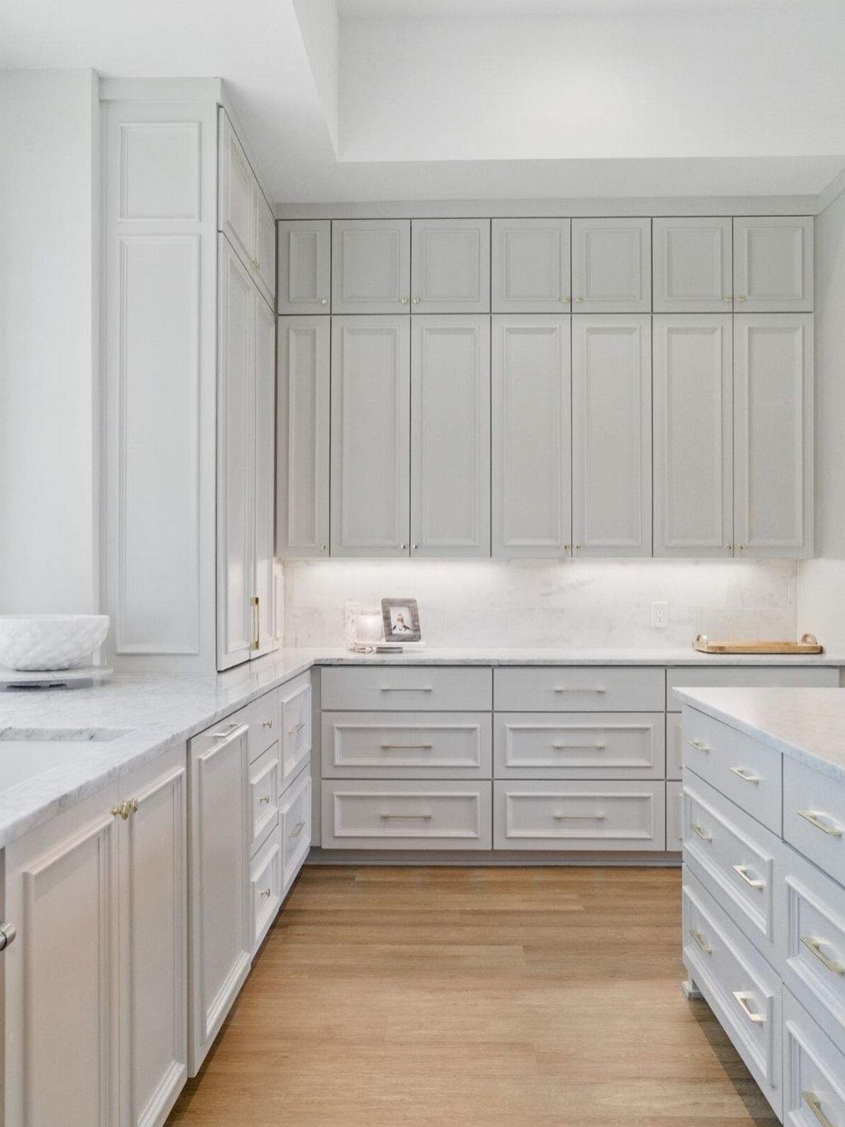 Light grey shaker kitchen cabinets with white marble countertops and light wood floors.