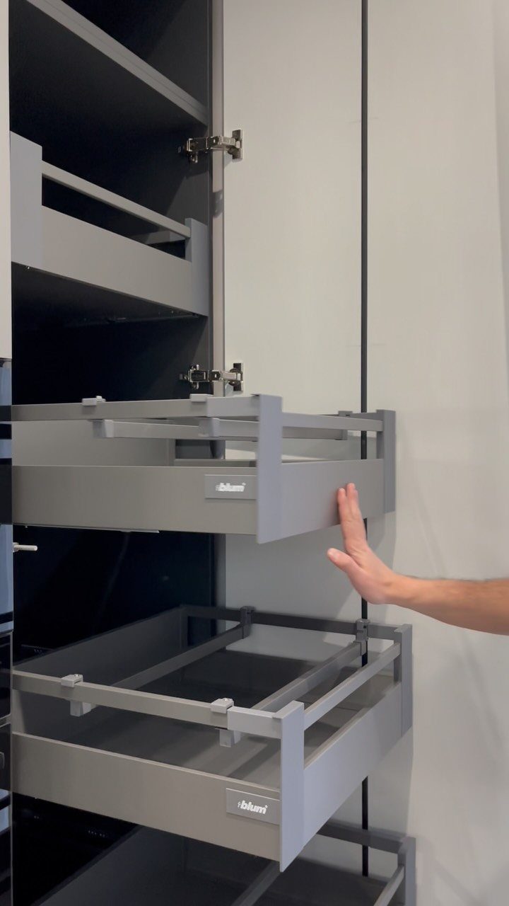 Grey pull-out kitchen cabinet drawers being opened by a person's hand.