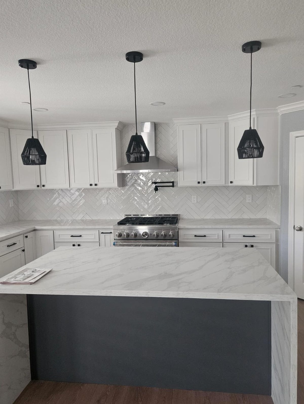 Modern kitchen with white cabinets, marble island, and a white textured tile backsplash.