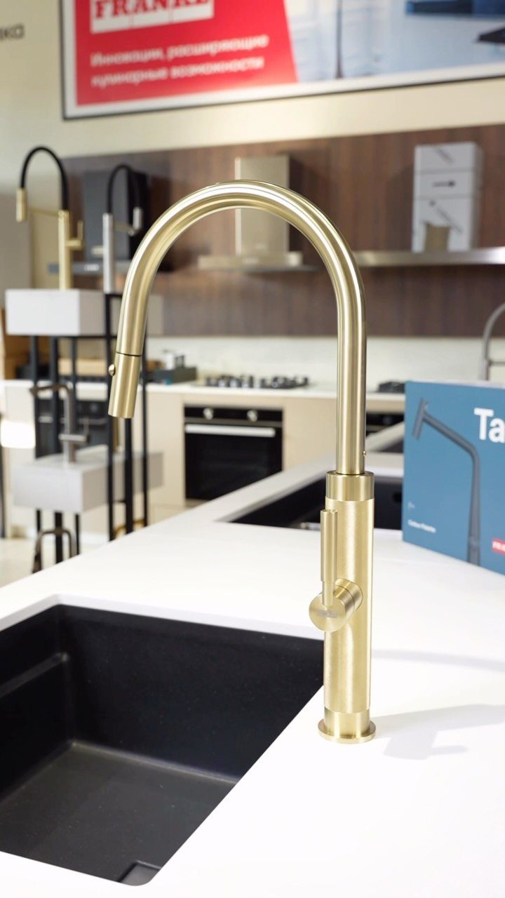Brushed gold high-arc kitchen faucet installed on a white countertop with black sink.