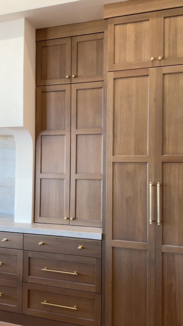Medium-toned wood kitchen cabinets with recessed panels and elegant gold hardware handles.