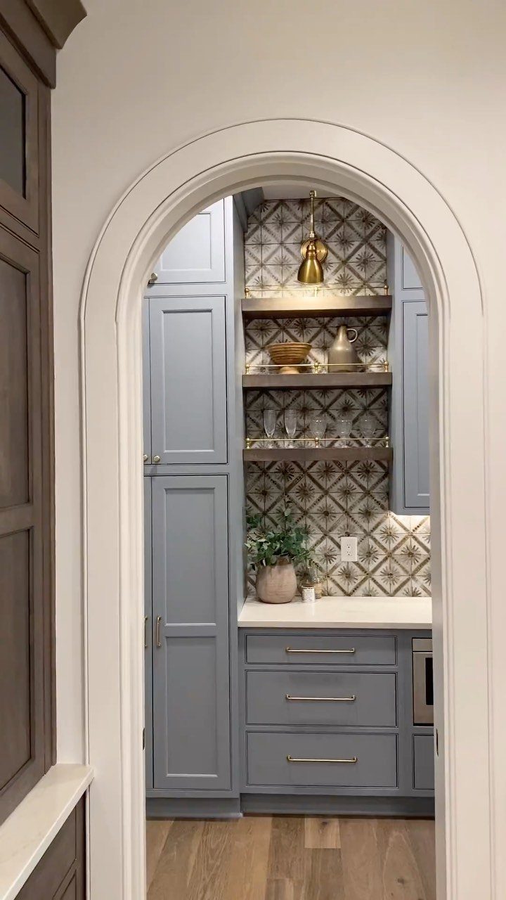 Arched doorway leading to a butler's pantry with blue cabinets and patterned tiles.