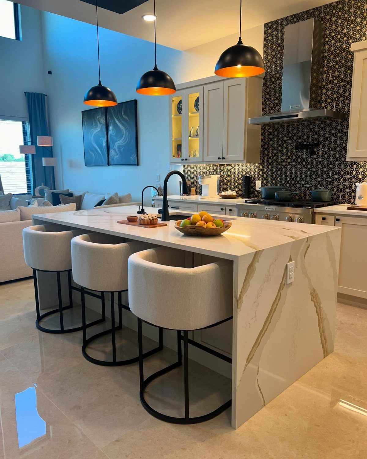 Large white marble kitchen island with three beige bar stools and black pendant lighting.