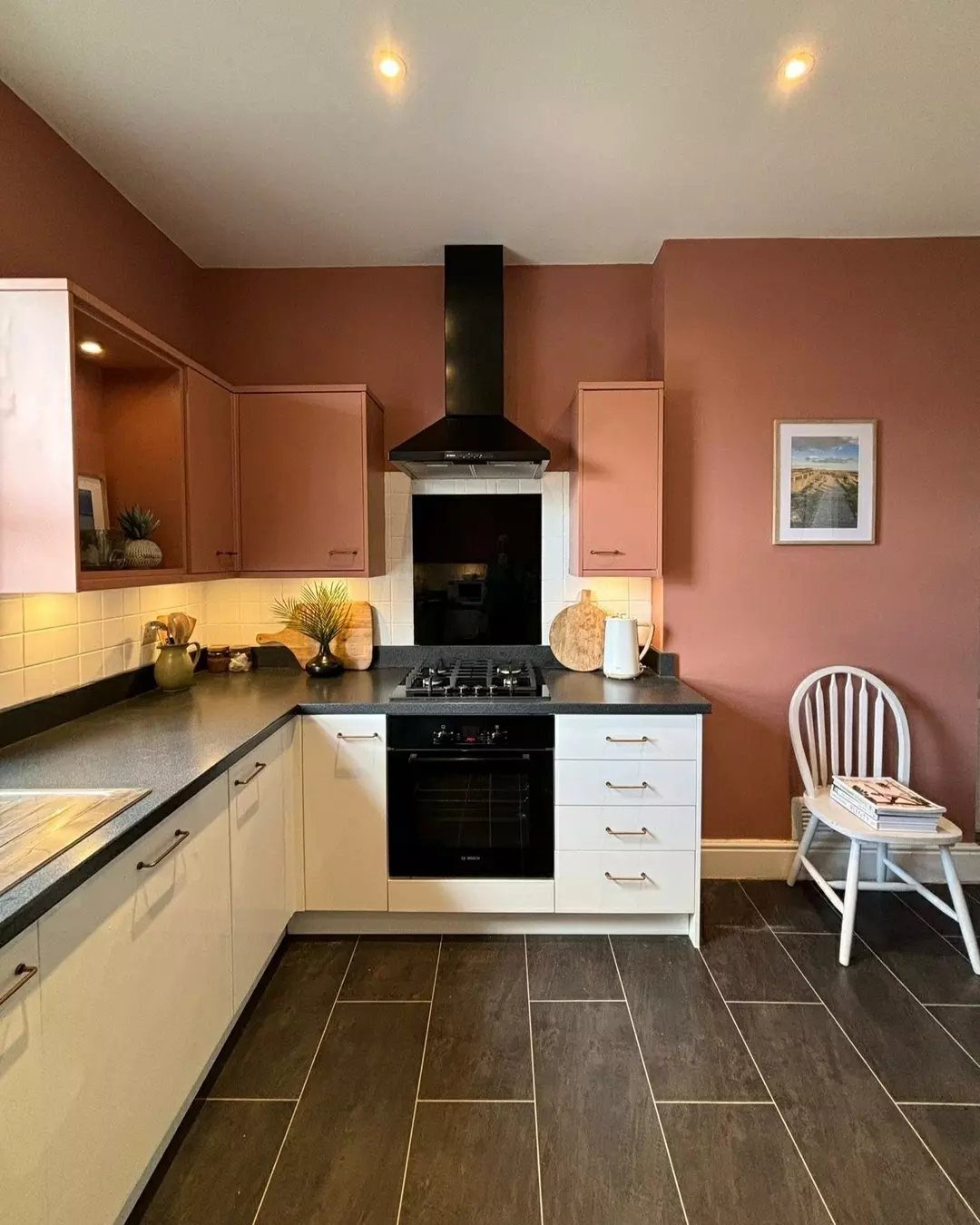 Terracotta painted accent wall in a kitchen with white cabinets and dark floors.