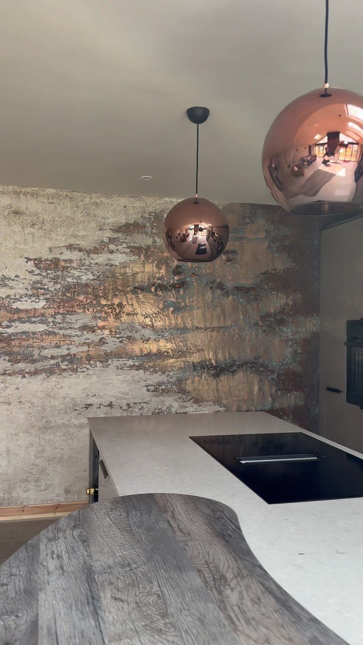 Textured metallic gold accent wall in a kitchen with copper pendant lights.