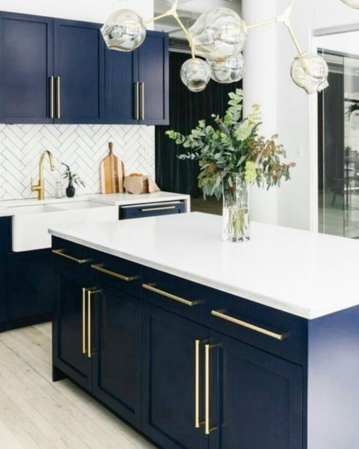Navy blue kitchen cabinets with gold hardware and white herringbone tile backsplash.