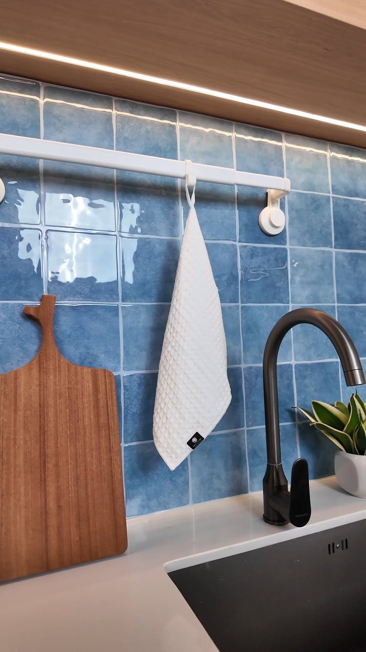 Glossy blue square glass tiles as a kitchen backsplash with a black faucet.