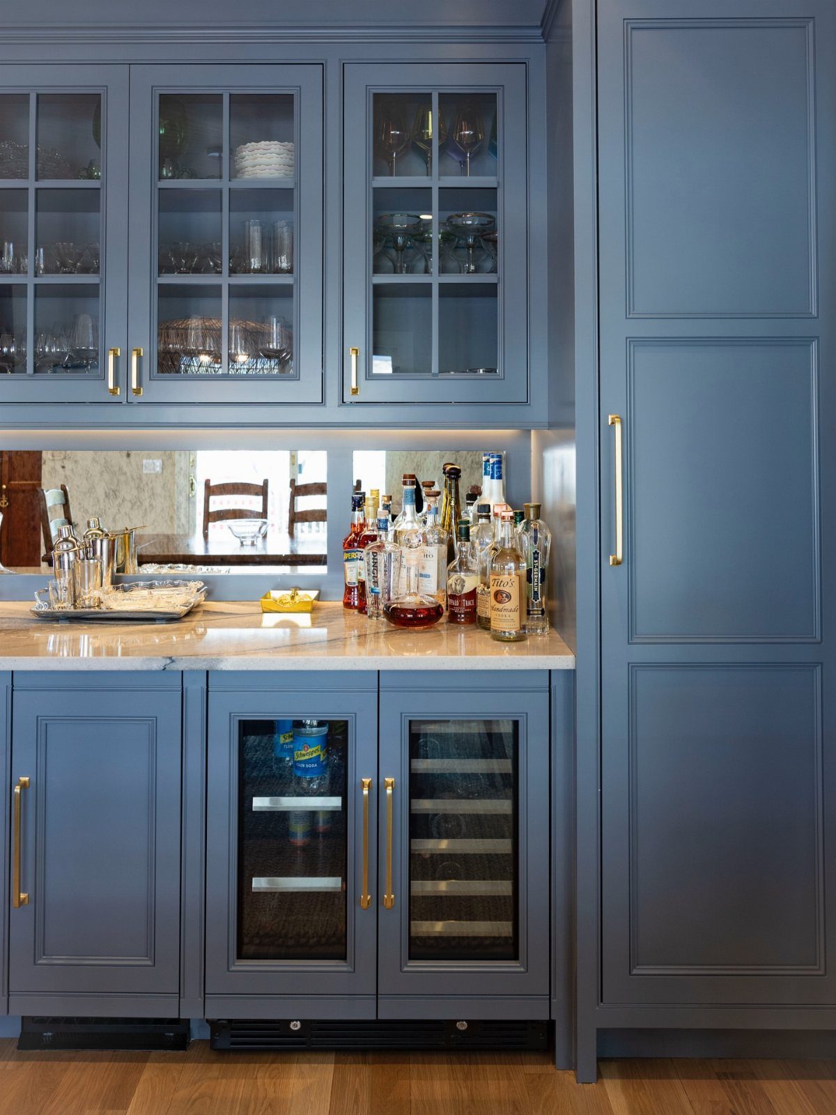 Dusty blue kitchen cabinets with gold hardware and a mirrored backsplash bar area.