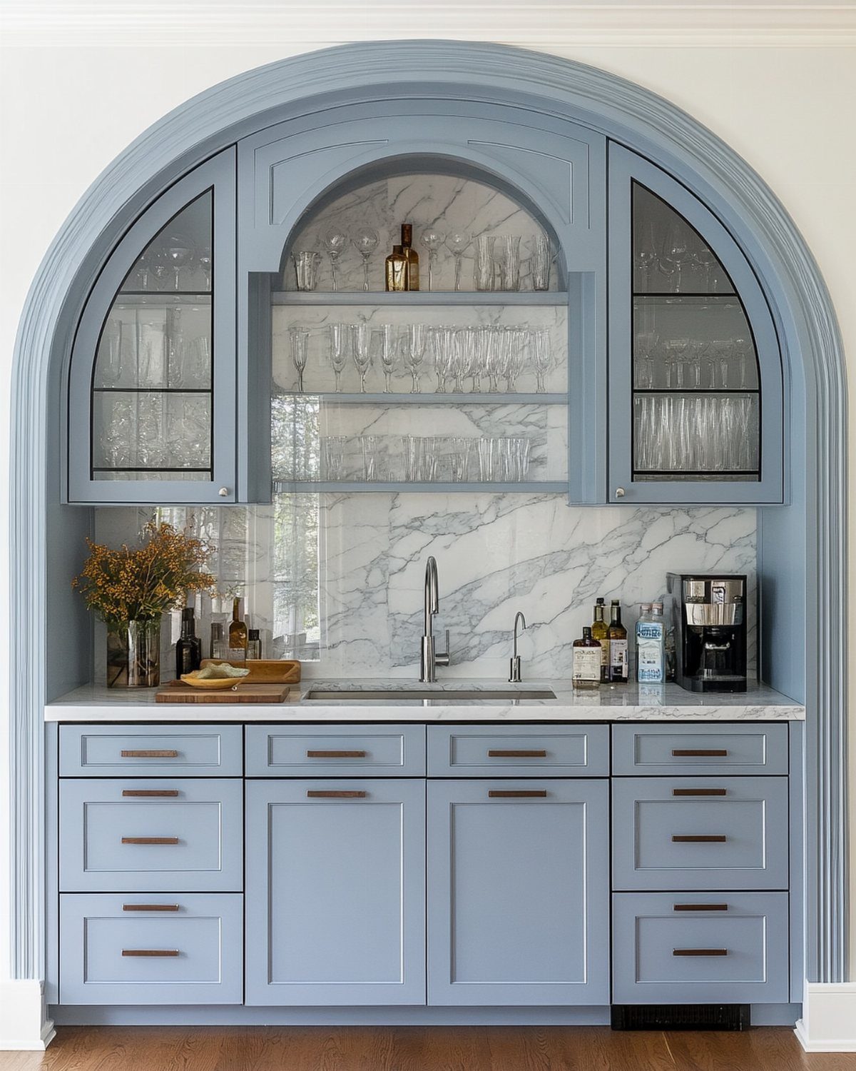 Light blue kitchen cabinets with a white marble backsplash and arched cabinetry.