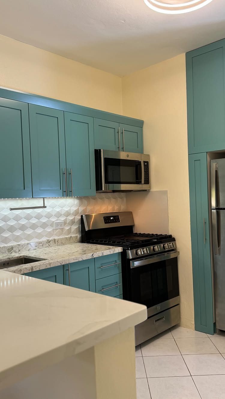 Turquoise blue kitchen cabinets with a white textured backsplash and stainless steel appliances.