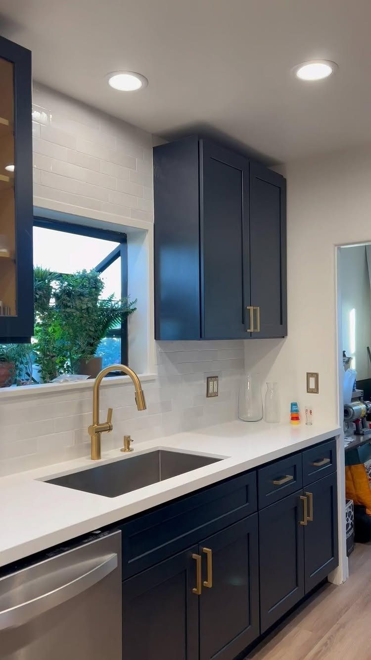 Navy blue kitchen cabinets with gold hardware and a white subway tile backsplash.