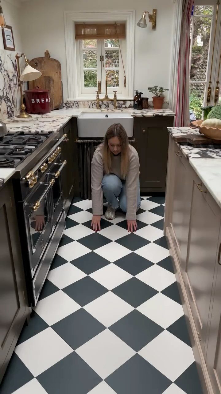 Woman crouching in a kitchen with black base cabinets and checkerboard flooring