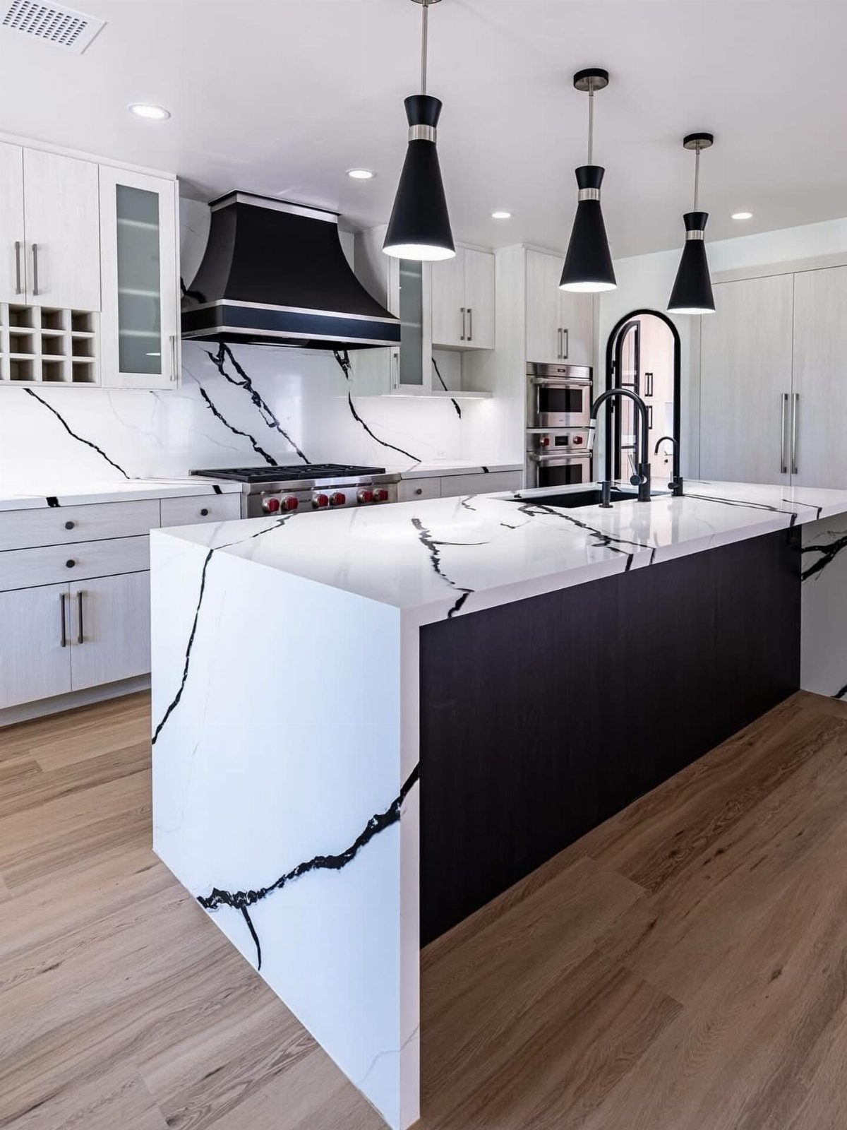 Modern kitchen with white waterfall island, black cabinets, and black pendant lights.