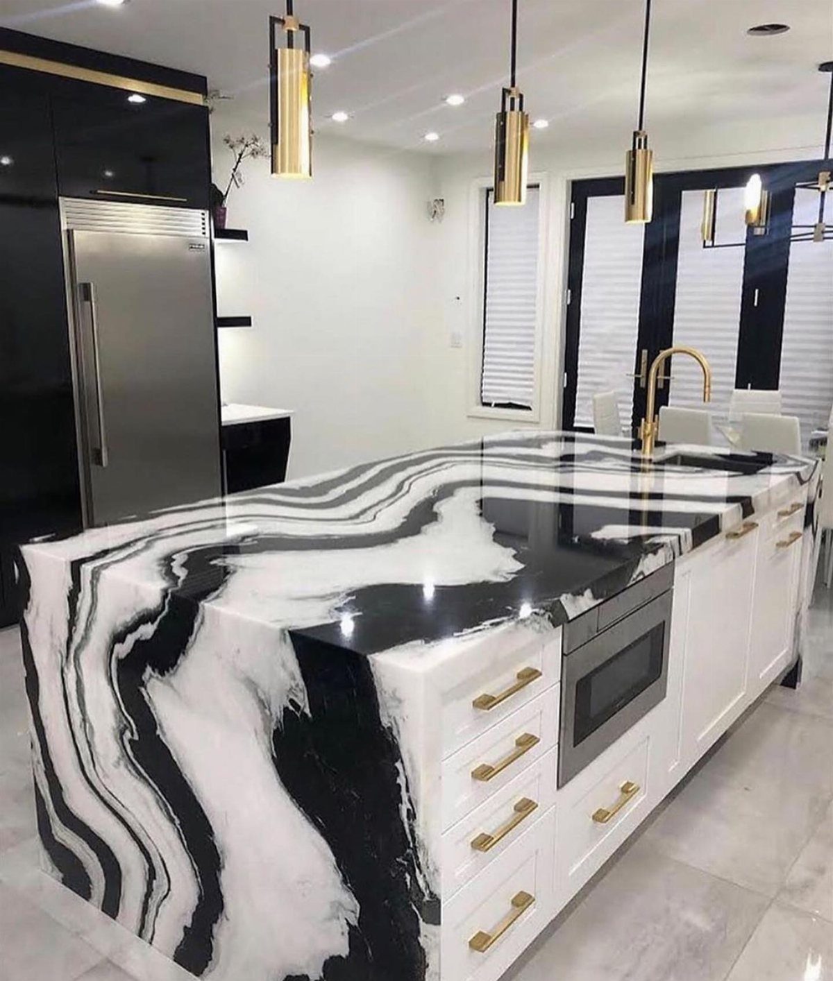 Marbled black and white waterfall island countertop with white cabinets and gold hardware