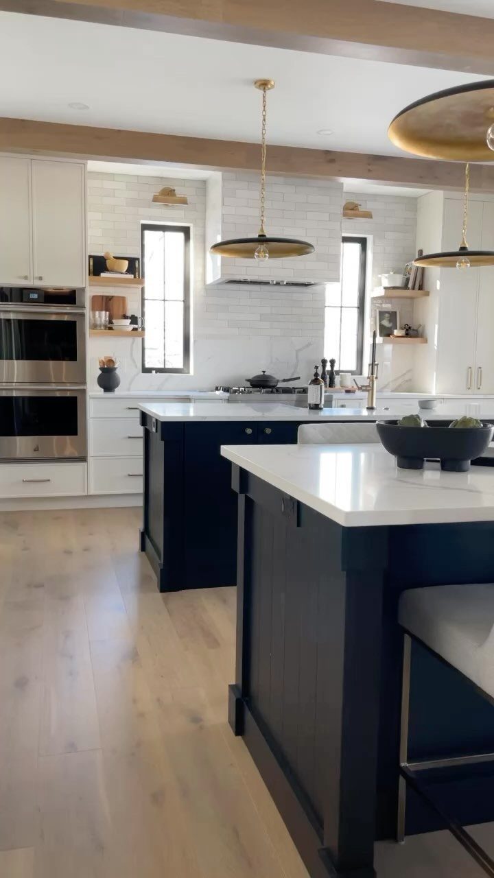 Black kitchen islands with white countertops in a bright white kitchen with wood accents