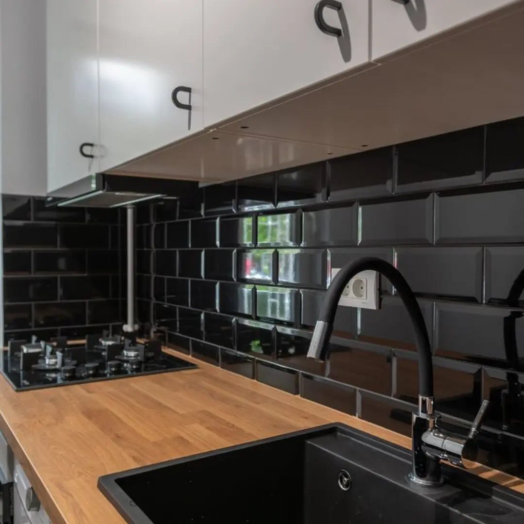 White kitchen cabinets and black subway tile backsplash with light wood countertops.