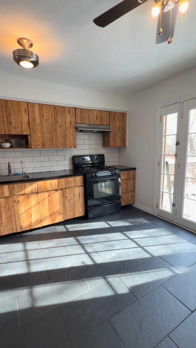 Kitchen with wooden cabinets, white subway tile backsplash, and black tiled flooring.