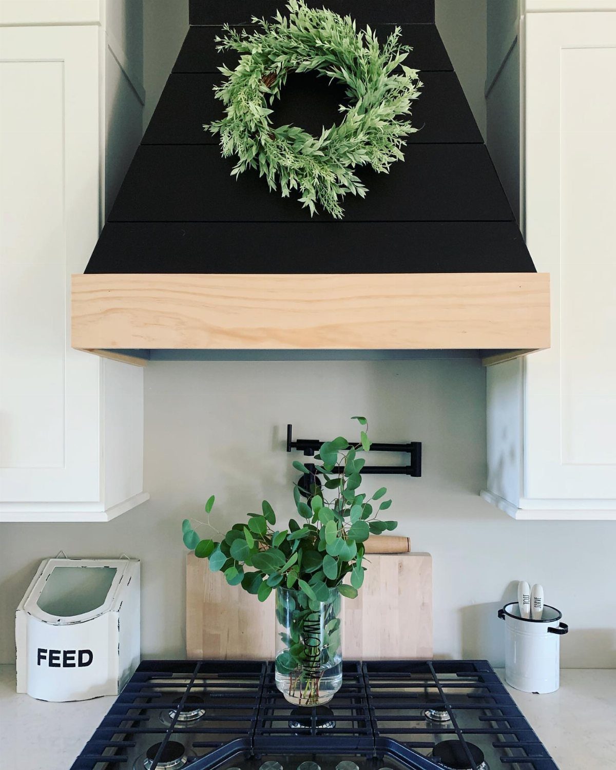 Black wooden range hood with light wood trim and a green wreath decoration.