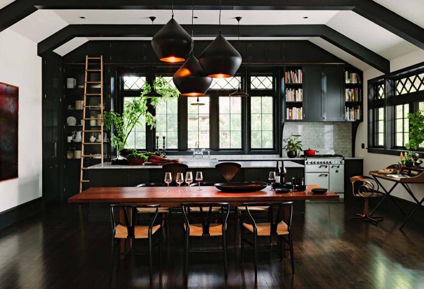 Modern kitchen with black cabinets, a large wooden dining table, and green plants.