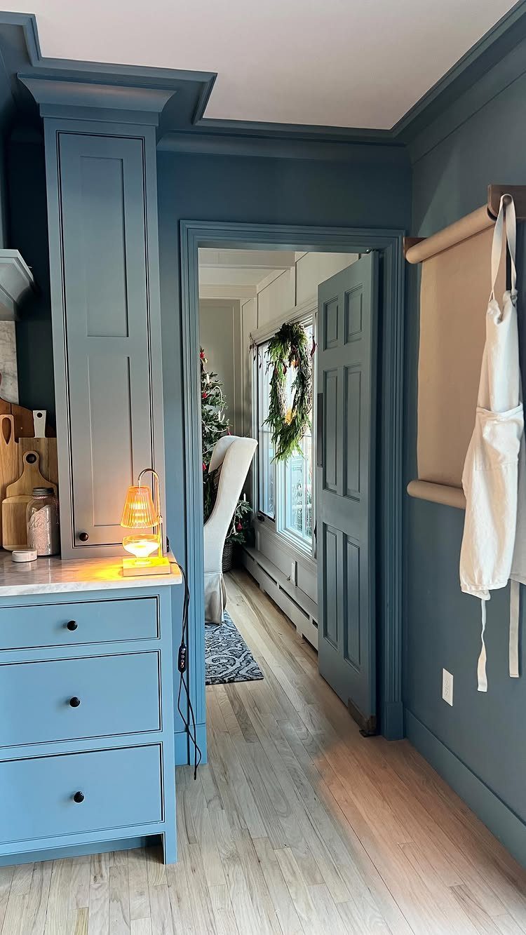 Medium blue-gray kitchen cabinets and walls with light wood flooring and white countertops.