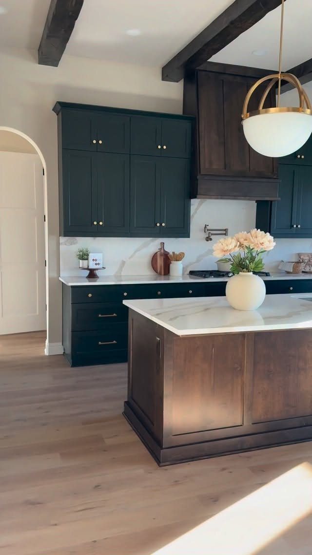 Deep blue-green kitchen cabinets with white marble countertops and a dark wood island.