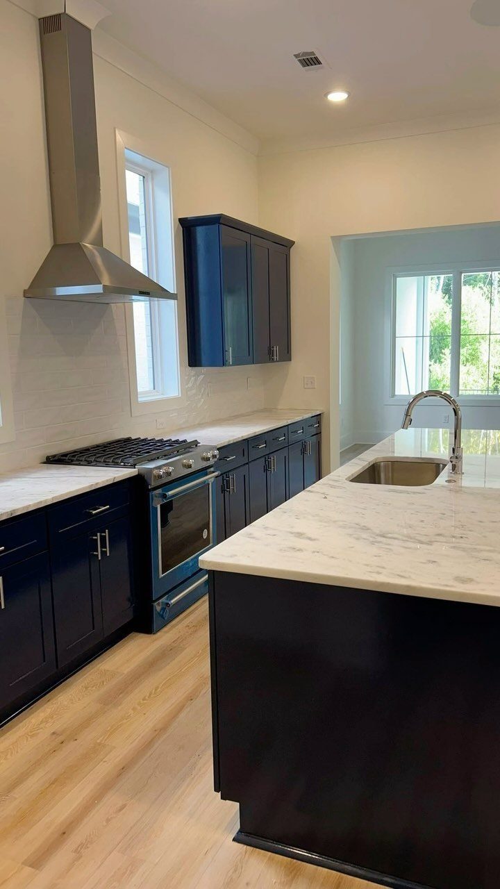 Navy blue kitchen cabinets with white marble countertops and light wood floors.