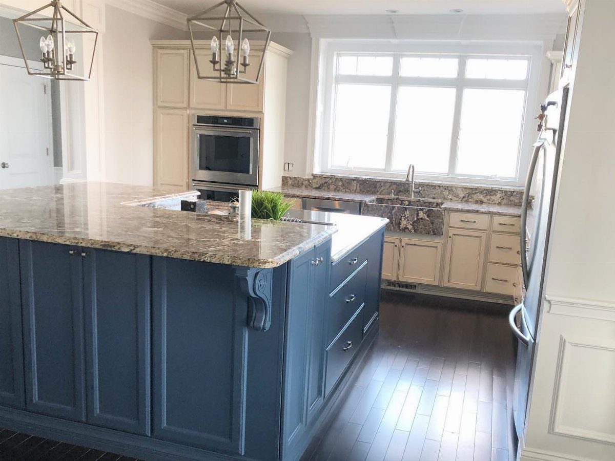 Deep blue kitchen island with granite countertops and cream background cabinetry.