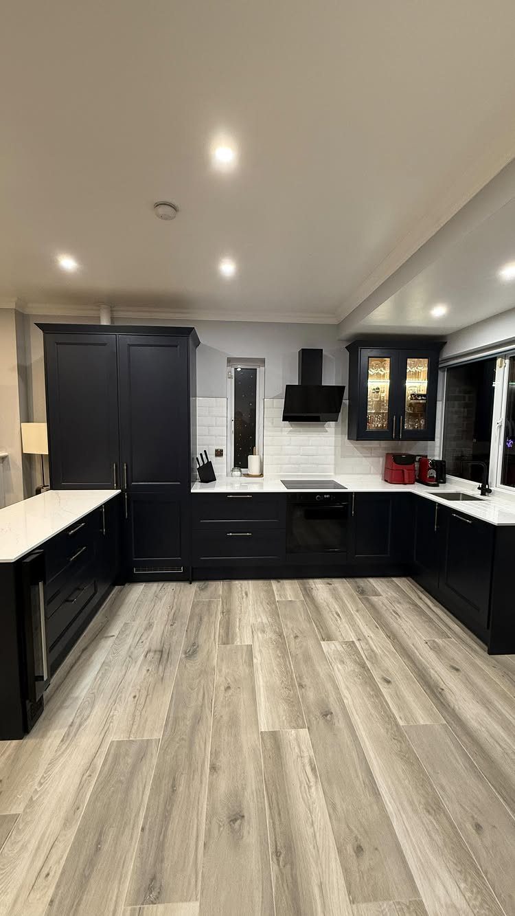 Navy blue kitchen cabinets with white countertops and light wood flooring.