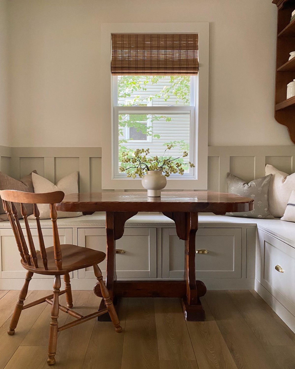 Light grey painted storage bench in a breakfast nook with a wooden table.
