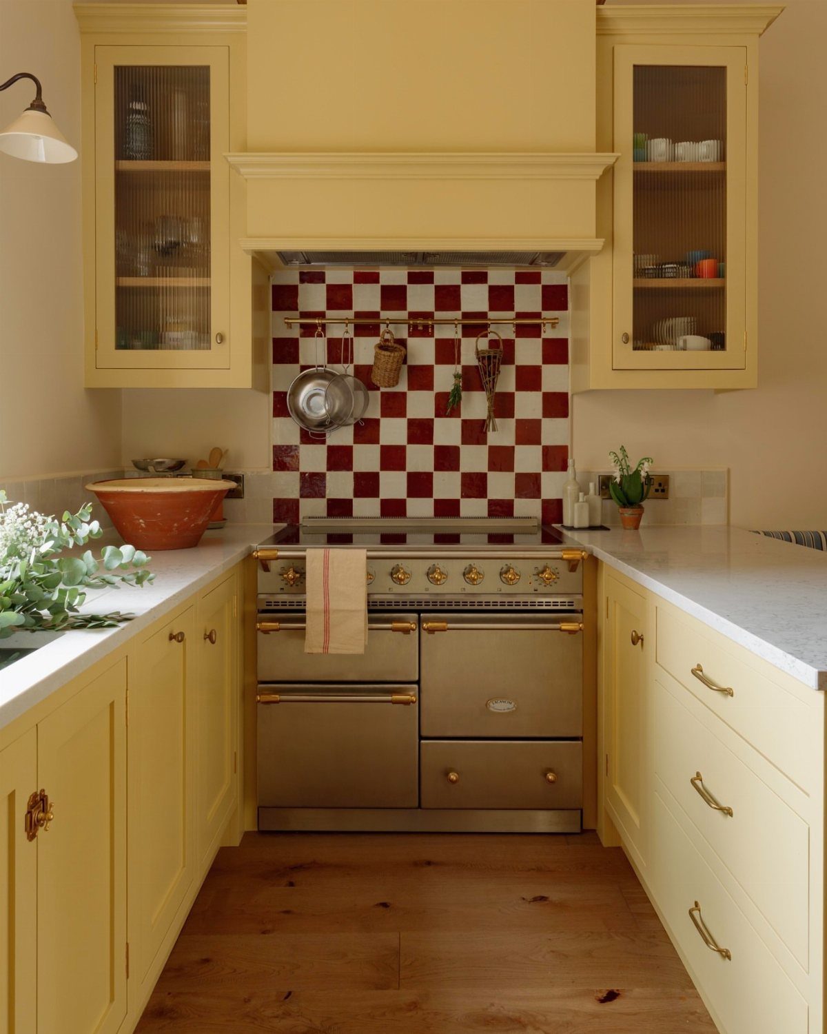 Butter yellow cabinetry framing a stainless steel range cooker with red checkered backsplash.