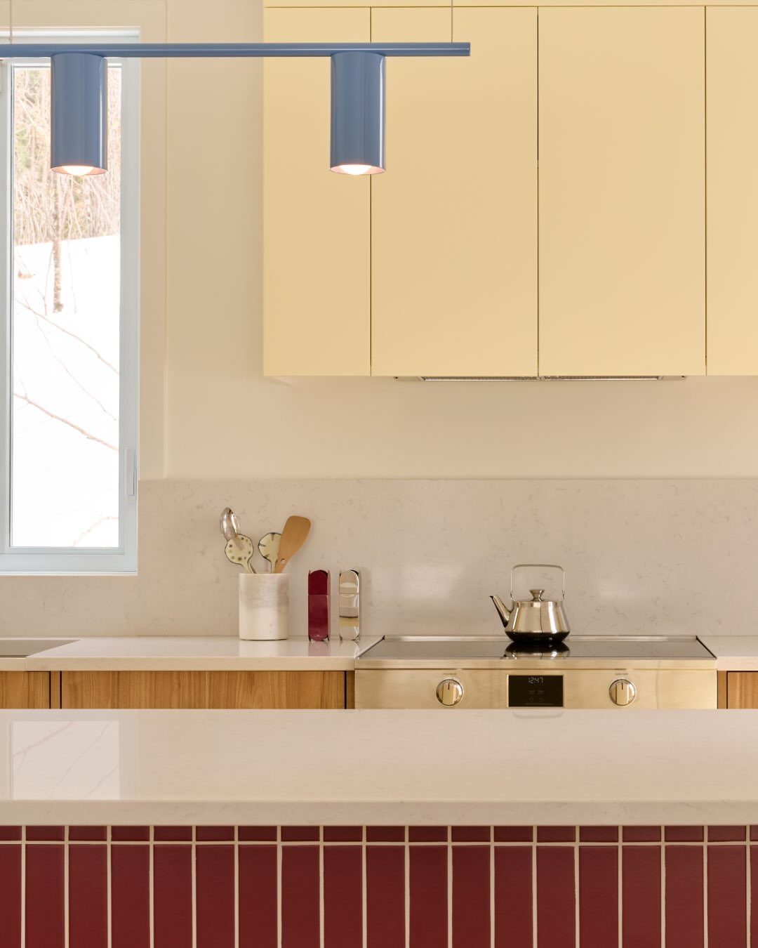 Pale yellow upper cabinets and deep burgundy tiled island in a modern kitchen.