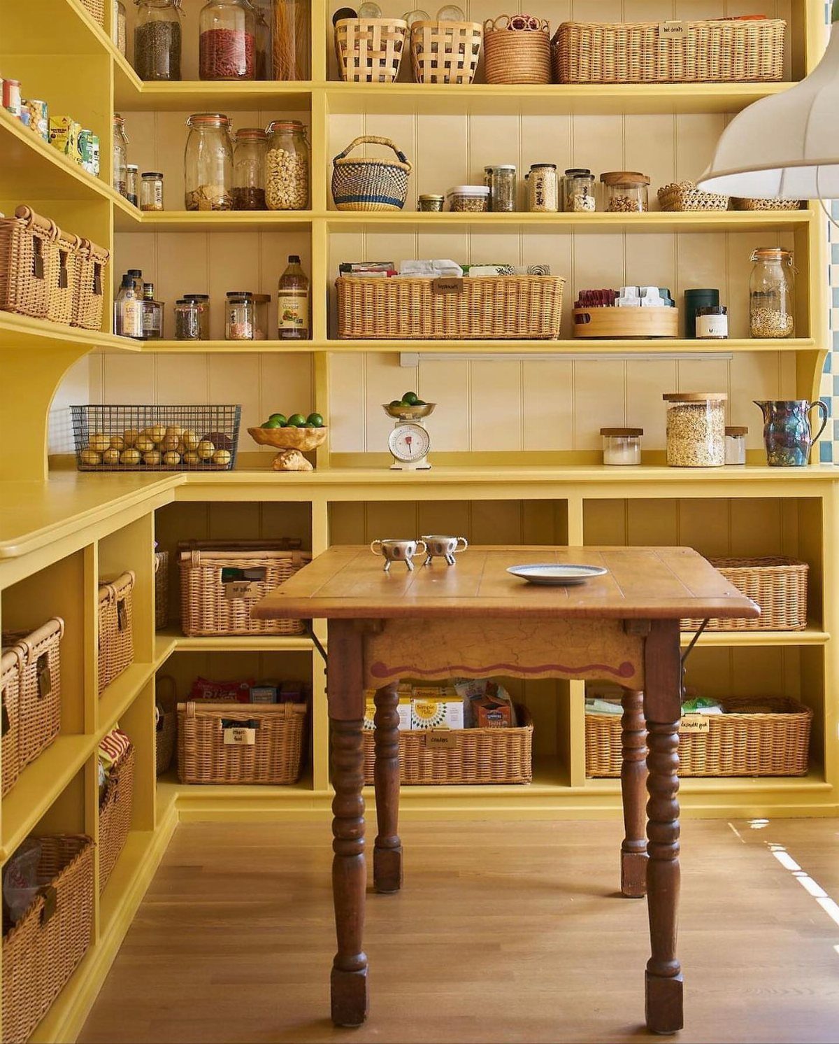 Butter yellow open kitchen shelving with wicker baskets and a wooden table.