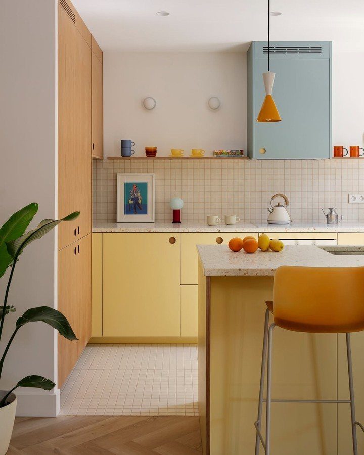 Butter yellow lower kitchen cabinets and island with light wood and blue cabinetry.