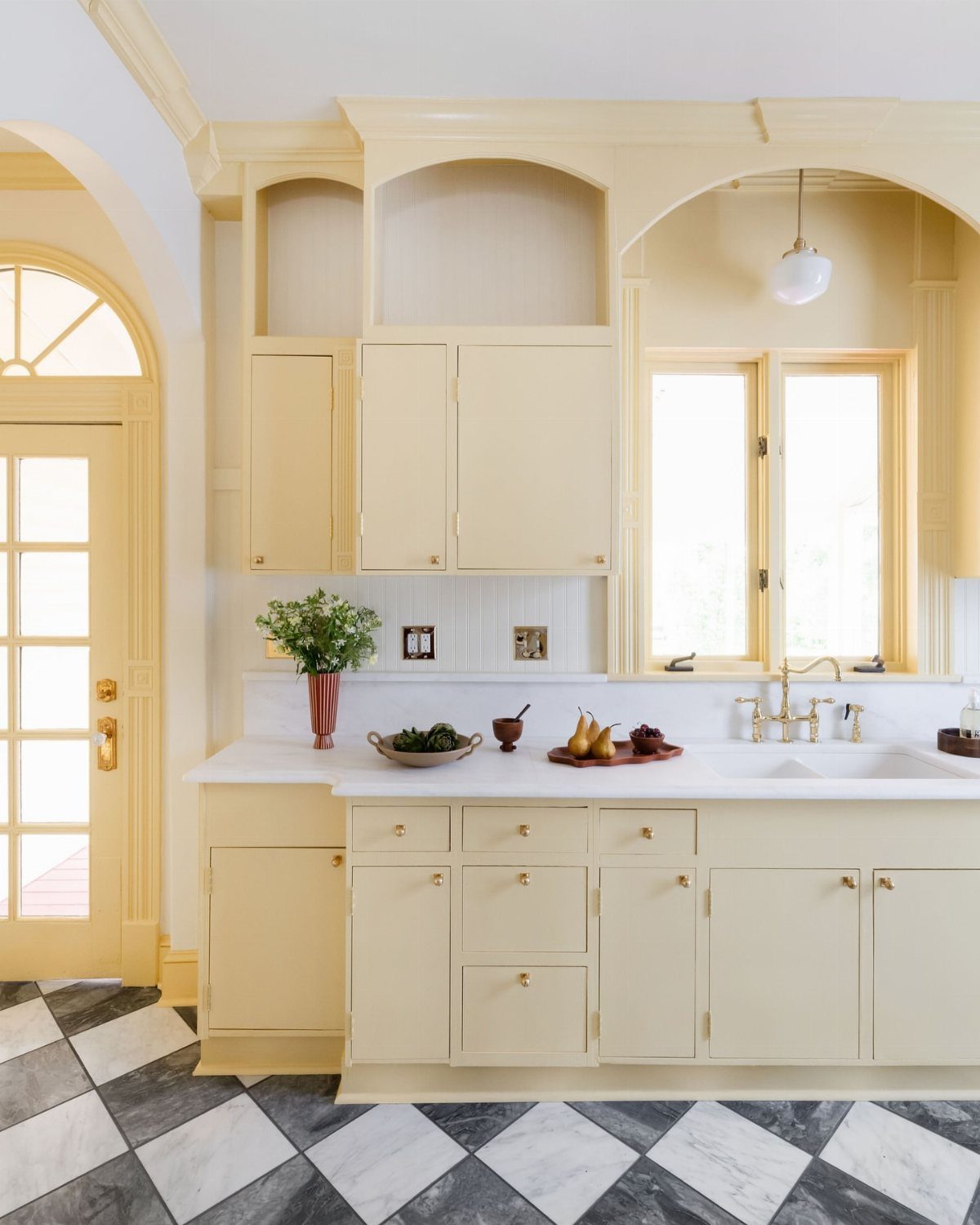 Butter yellow kitchen cabinets with white countertops and checkered marble flooring.