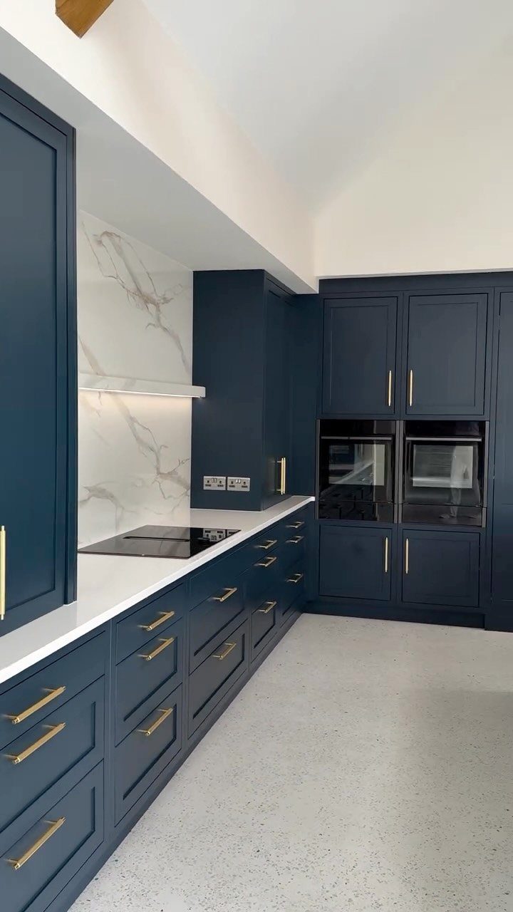 Dark blue-green kitchen cabinets with gold handles and white marble backsplash.