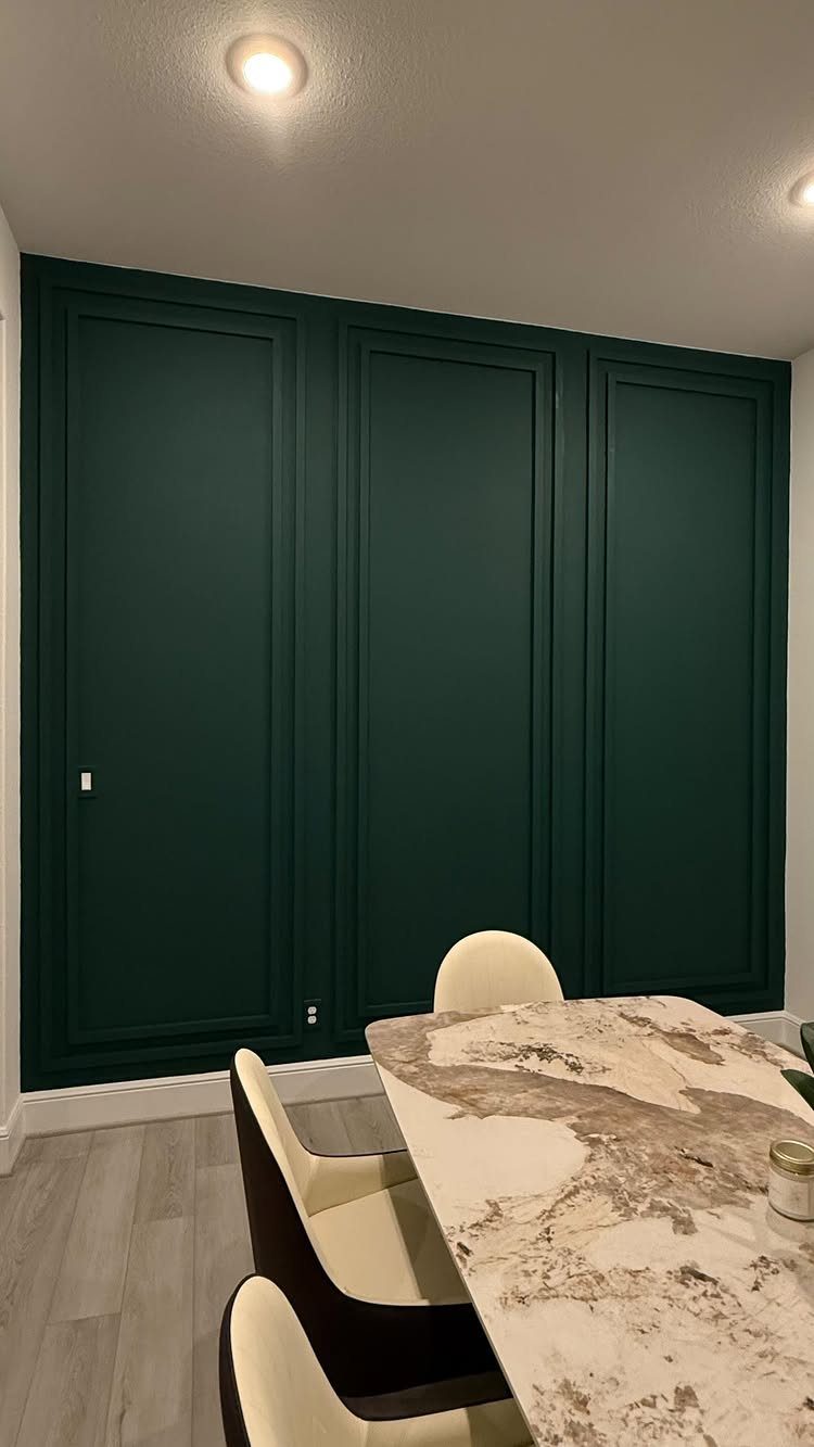 Dark green accent wall with molding panels behind a marble dining table.