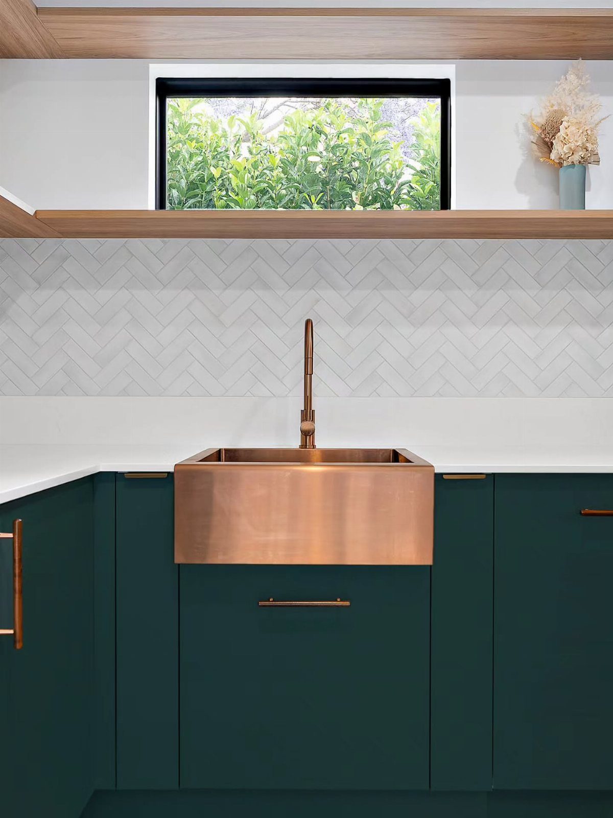 Dark green kitchen cabinets featuring a copper farmhouse sink and white herringbone backsplash.
