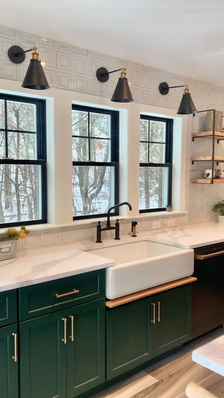 Dark green kitchen cabinets with gold hardware and a white farmhouse sink.