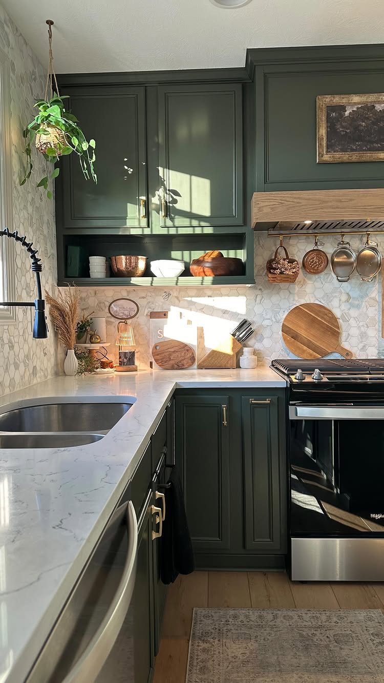 Dark green kitchen cabinets with white marble countertops and a hanging indoor plant.