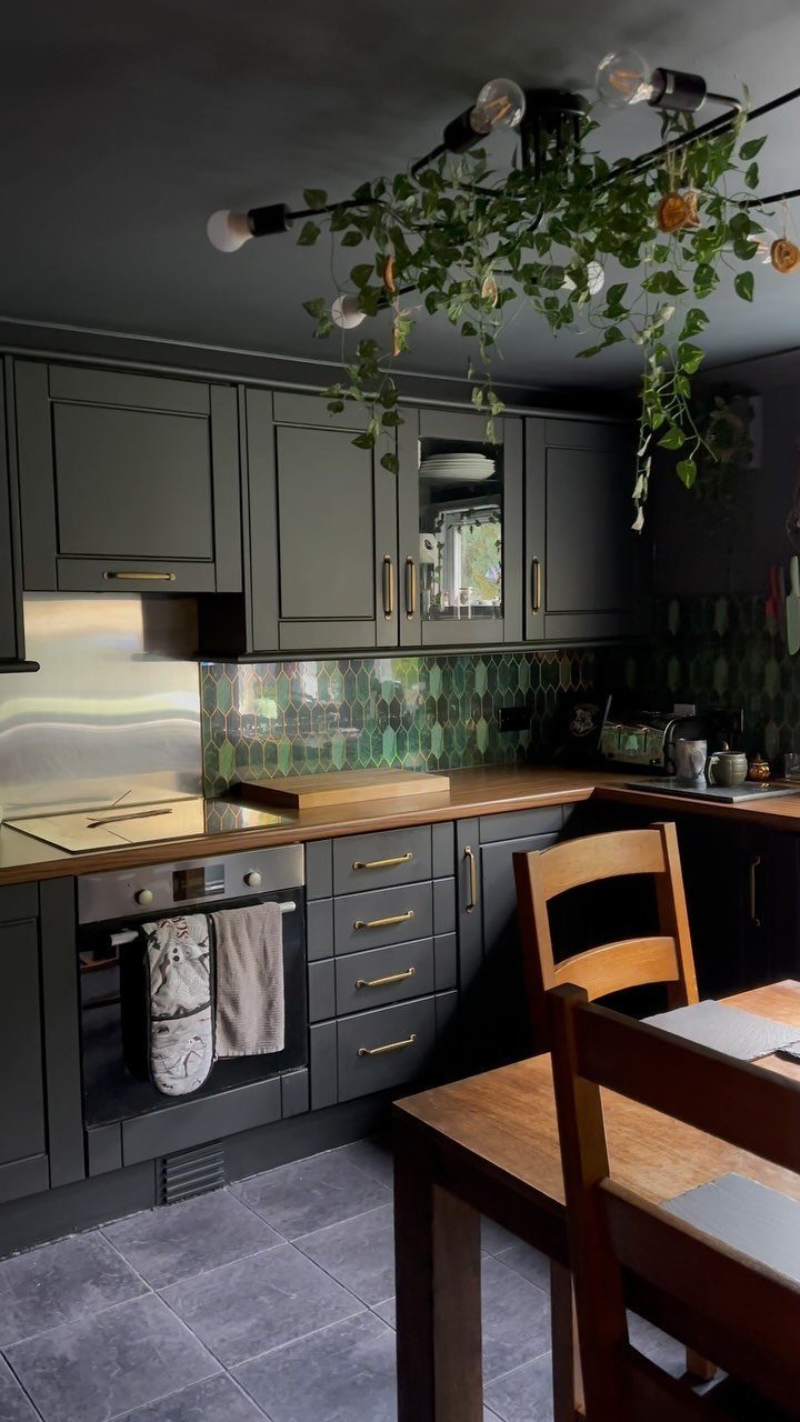 Dark green kitchen cabinets with a green patterned tile backsplash and wooden countertops.