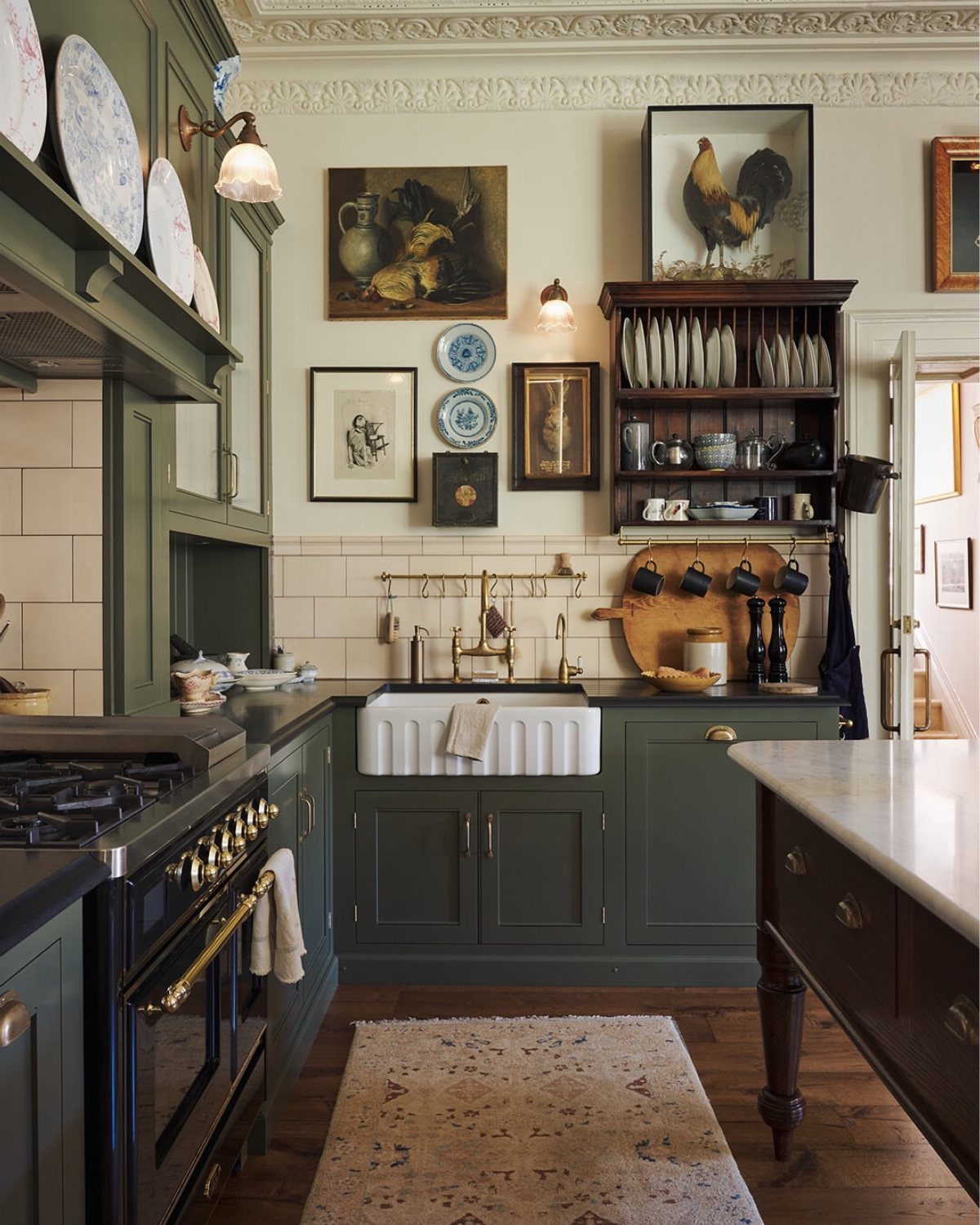 Dark green kitchen cabinets with brass vintage fixtures and a white farmhouse sink.