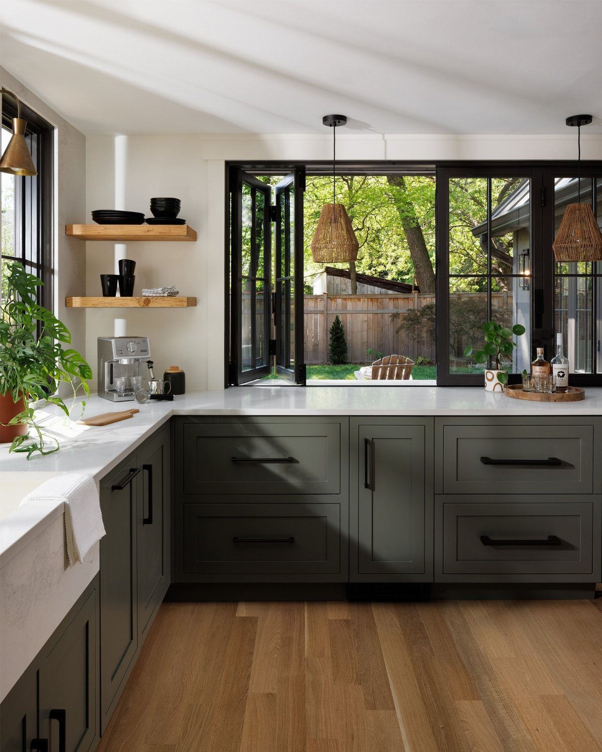 Dark forest green kitchen cabinets with white countertops and light wood floors.