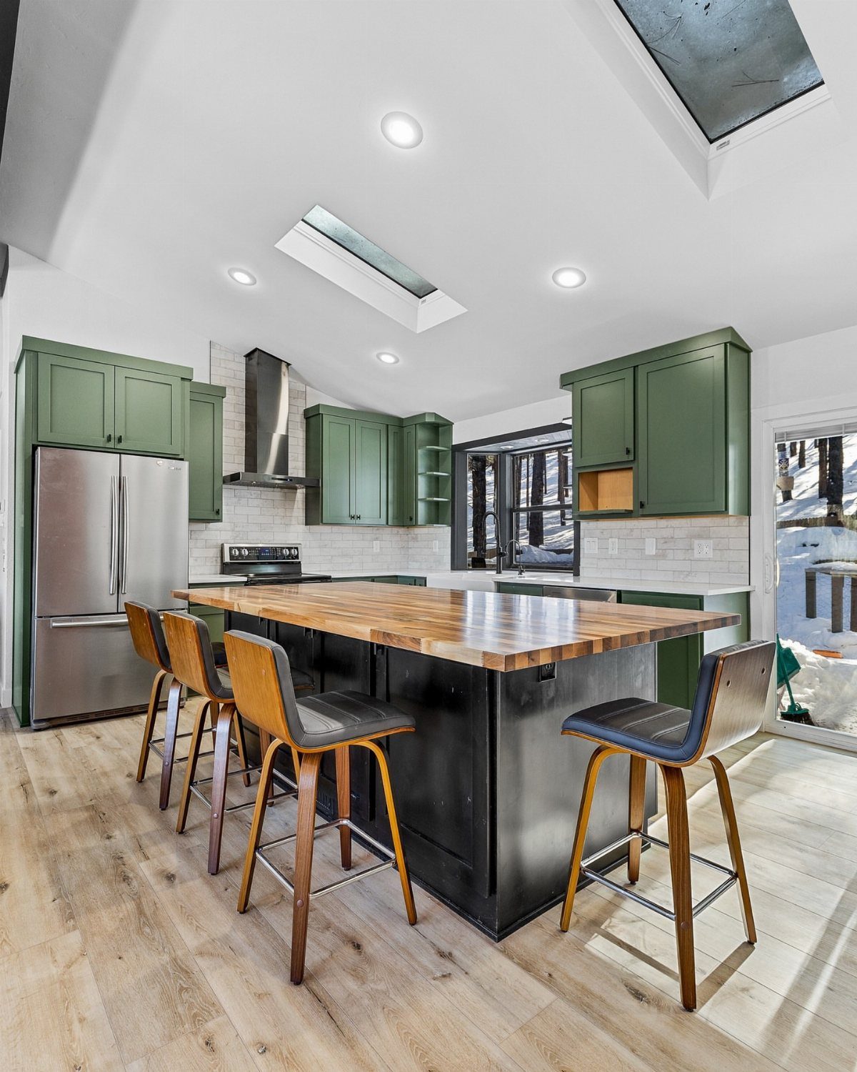 Earthy green kitchen cabinets with a black island and wooden countertop and stools.