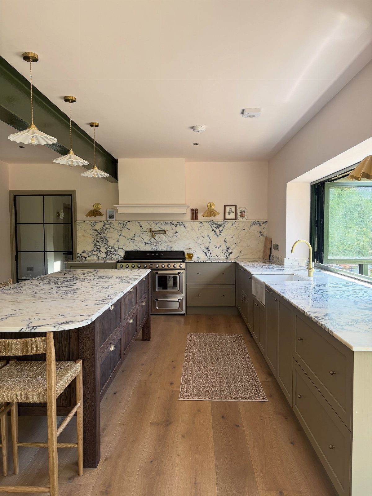 Olive green kitchen cabinets with white and gray marble countertops and wood floors.