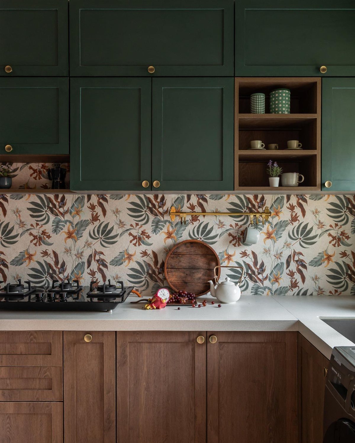Dark green upper cabinets and wood lower cabinets with botanical leaf patterned wallpaper backsplash.