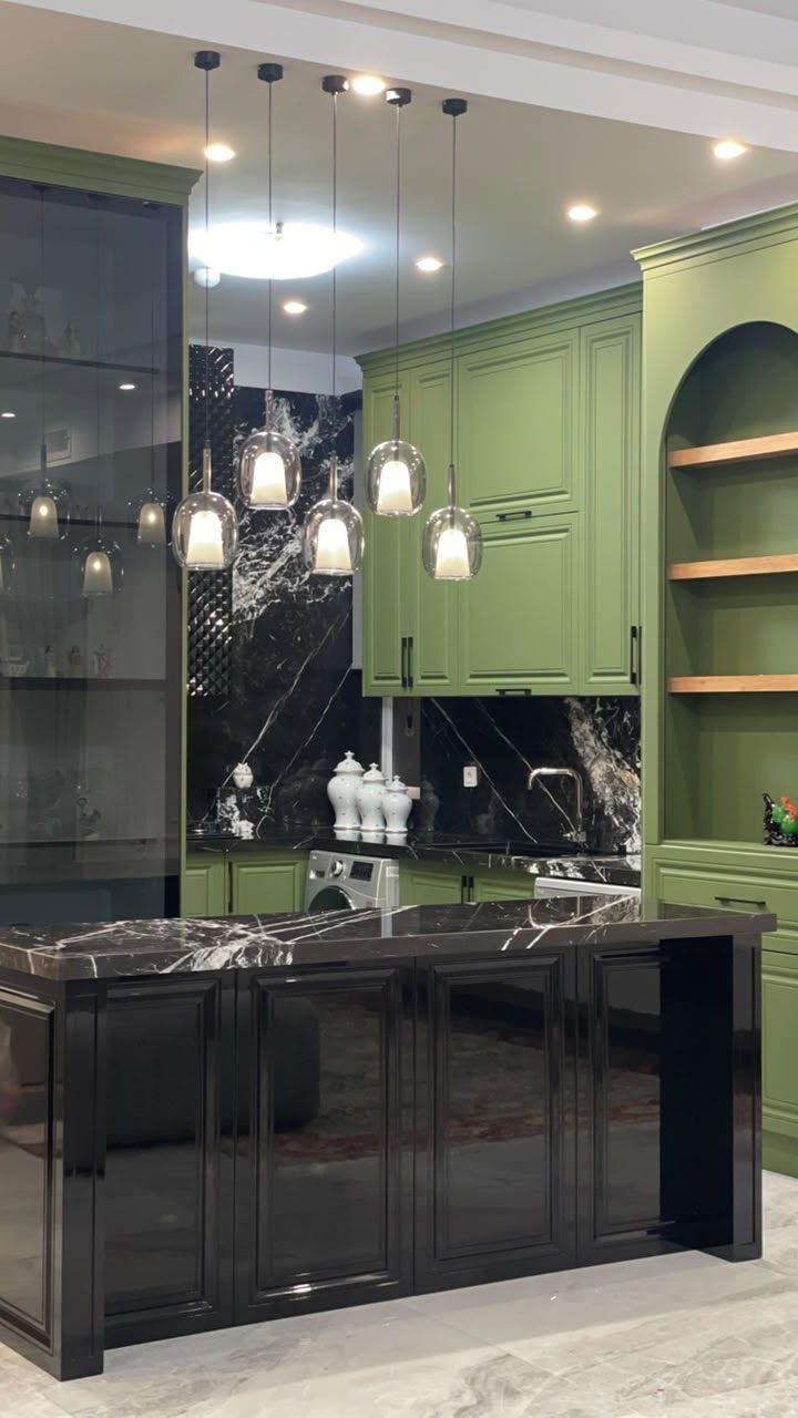 Olive green kitchen cabinets with black hardware and a black marble island.