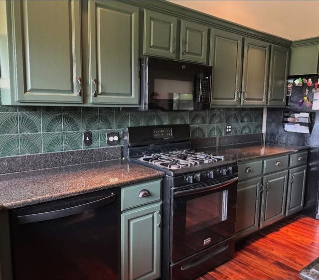 Sage green kitchen cabinets with dark countertops and a patterned green tile backsplash.