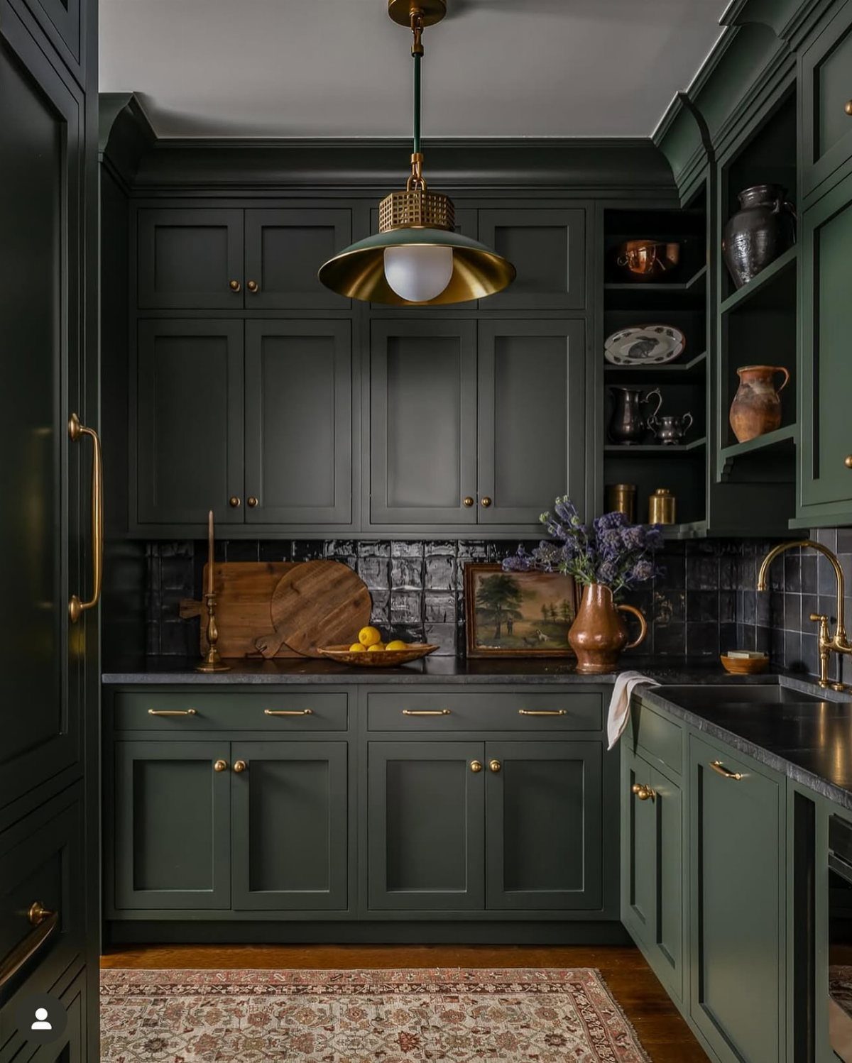 Dark green farmhouse kitchen cabinets with gold handles and a black tile backsplash.