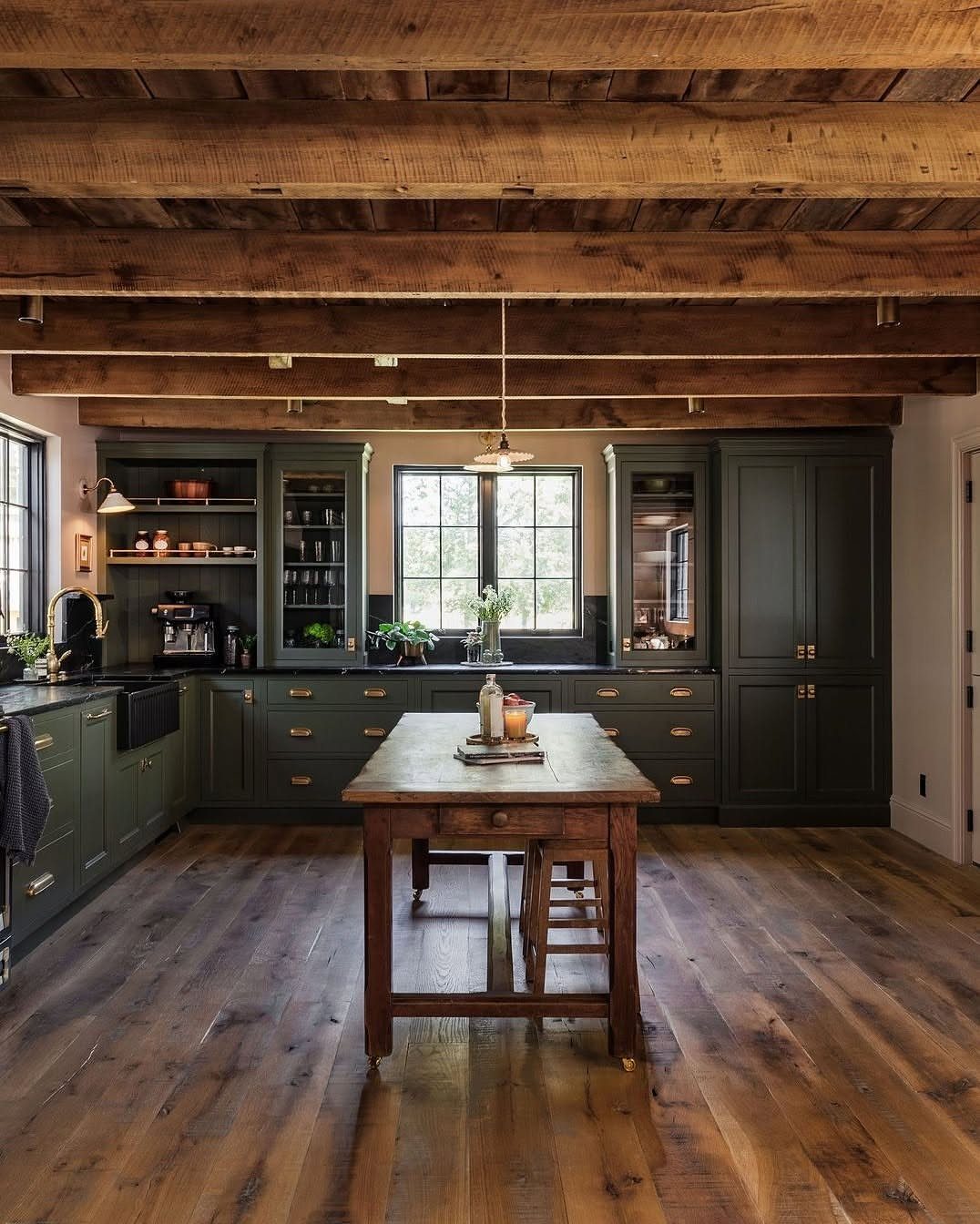 Dark green farmhouse kitchen cabinets with rustic wooden beams and hardwood floors.